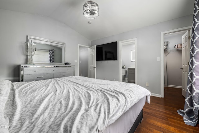 bedroom featuring dark wood finished floors, a spacious closet, vaulted ceiling, ensuite bath, and baseboards