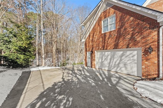 view of side of property featuring concrete driveway, brick siding, and an attached garage