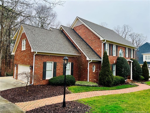 colonial-style house featuring a garage, brick siding, driveway, roof with shingles, and a front yard