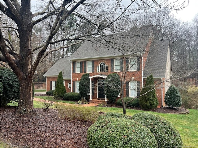 colonial-style house with a shingled roof, a front yard, and brick siding