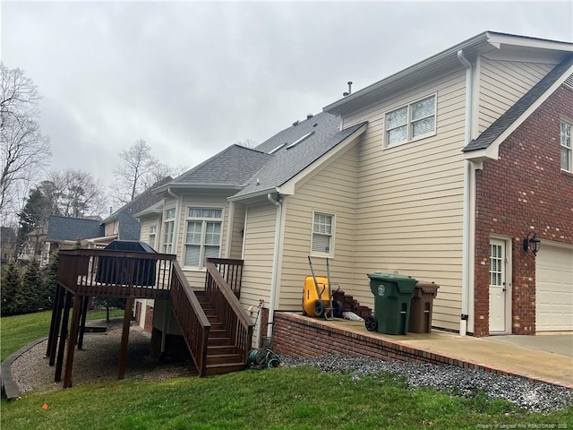 rear view of property featuring brick siding, a shingled roof, an attached garage, a wooden deck, and stairs