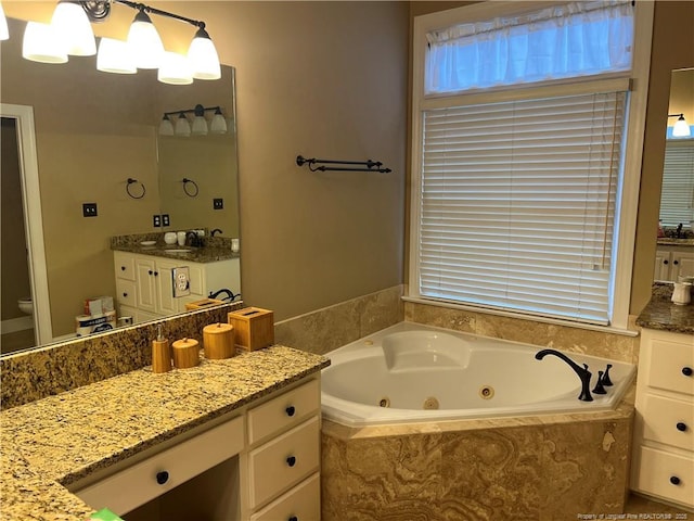 full bath with a notable chandelier, a jetted tub, toilet, and vanity