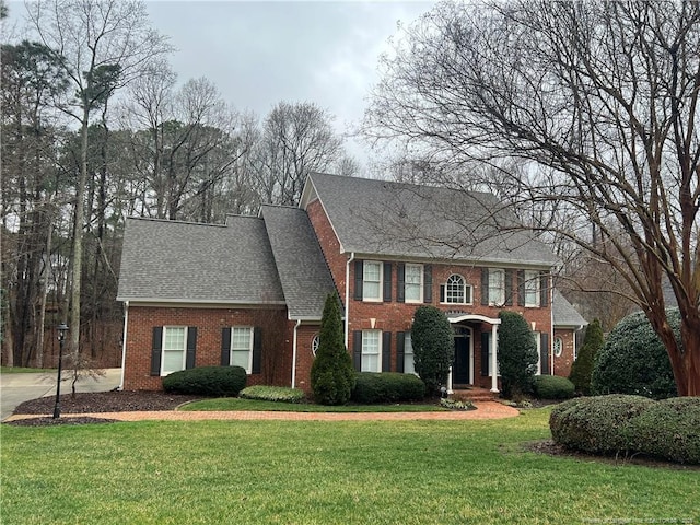 view of front facade featuring brick siding, roof with shingles, and a front yard