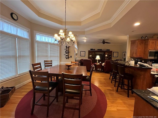 dining space featuring a tray ceiling, crown molding, light wood-style floors, baseboards, and ceiling fan with notable chandelier