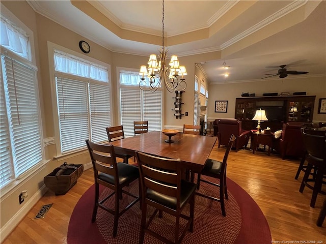 dining area featuring ceiling fan with notable chandelier, visible vents, light wood-style floors, ornamental molding, and a raised ceiling