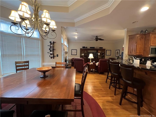 dining room featuring light wood-style flooring, a raised ceiling, crown molding, and ceiling fan with notable chandelier