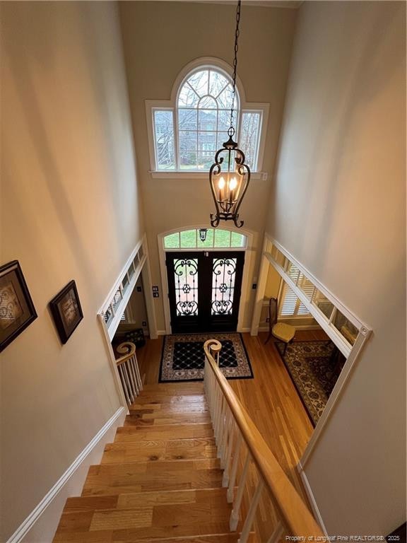 entrance foyer with a notable chandelier, stairway, a high ceiling, wood finished floors, and baseboards