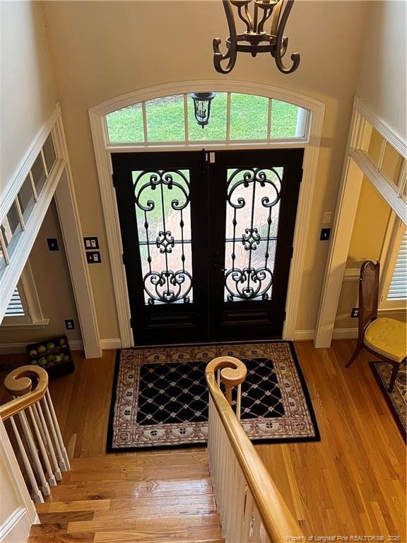 foyer entrance featuring baseboards, french doors, a towering ceiling, and light wood-style floors