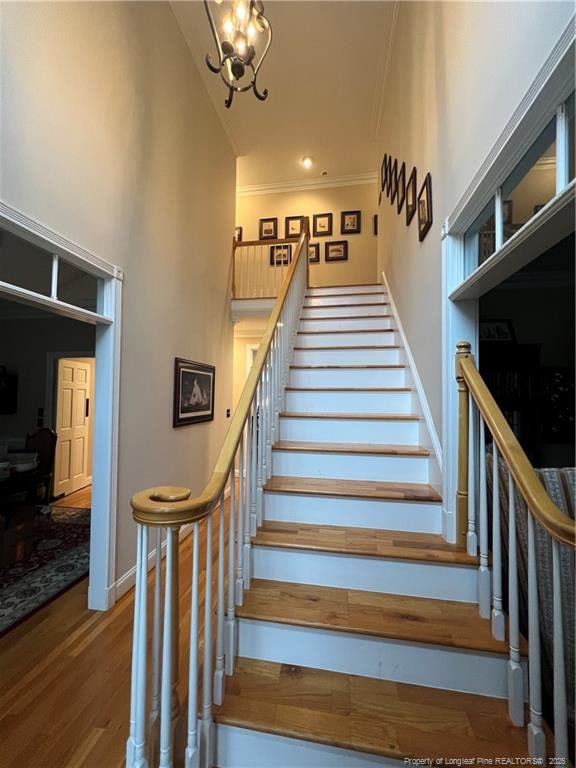 stairway featuring a notable chandelier, a high ceiling, ornamental molding, wood finished floors, and baseboards