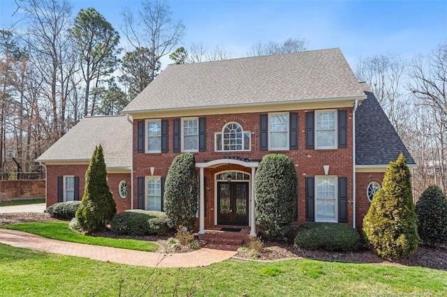 georgian-style home with a front lawn, french doors, brick siding, and roof with shingles