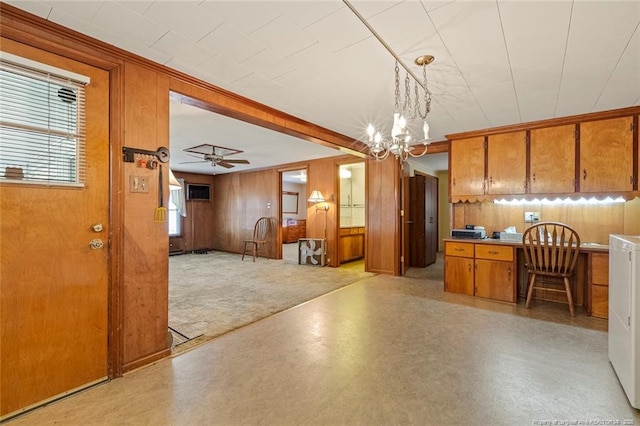 kitchen with pendant lighting, brown cabinetry, open floor plan, wooden walls, and ceiling fan with notable chandelier