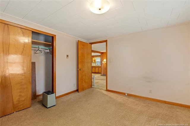 unfurnished bedroom featuring carpet floors, a closet, crown molding, and baseboards