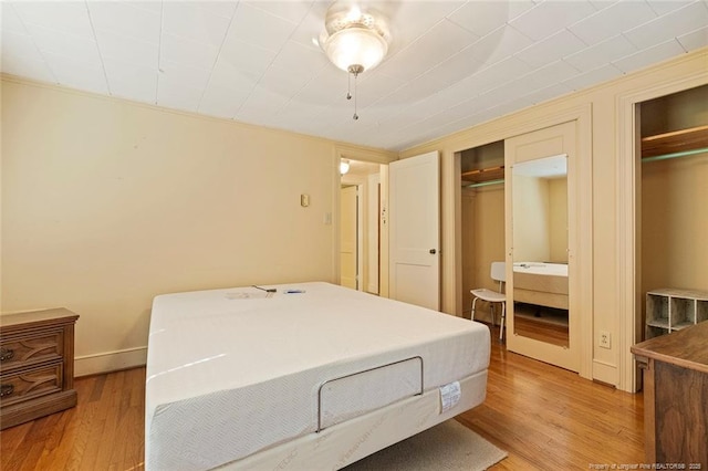 bedroom featuring multiple closets, light wood-type flooring, and baseboards