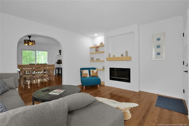 living area with arched walkways, a glass covered fireplace, wood finished floors, and recessed lighting