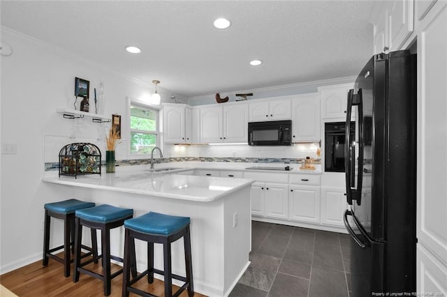 kitchen featuring white cabinets, a sink, a peninsula, and black appliances