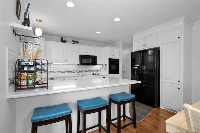 kitchen with a peninsula, wood finished floors, white cabinetry, a kitchen breakfast bar, and black appliances