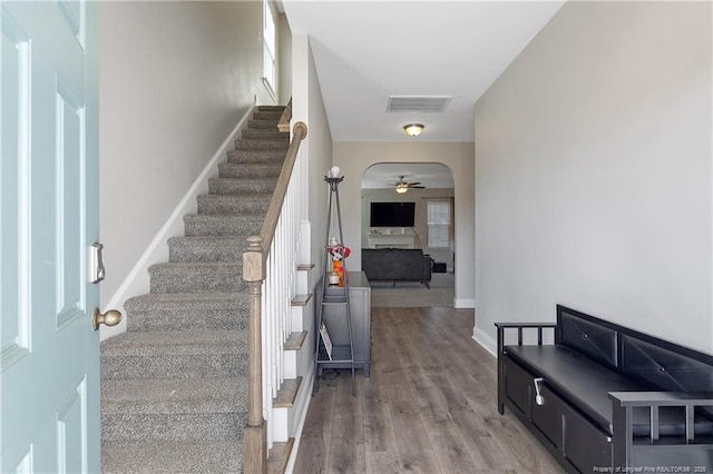 stairway featuring arched walkways, visible vents, ceiling fan, wood finished floors, and baseboards