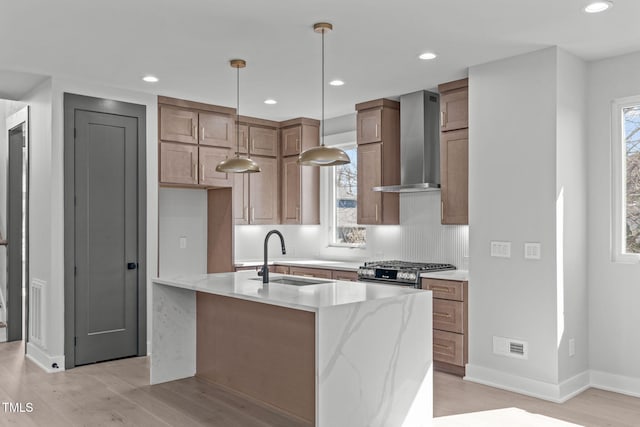 kitchen with visible vents, a healthy amount of sunlight, a sink, and wall chimney range hood