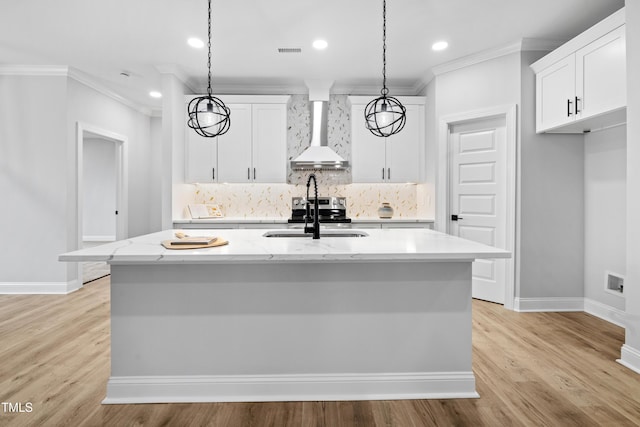 kitchen featuring visible vents, a kitchen island with sink, a sink, decorative backsplash, and wall chimney range hood