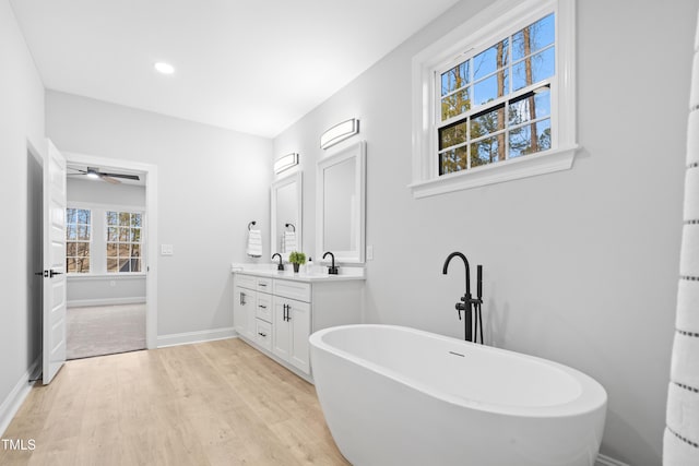 bathroom featuring baseboards, double vanity, wood finished floors, a soaking tub, and a sink