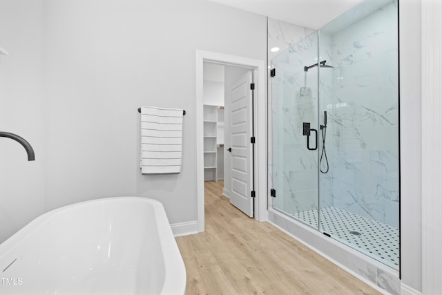 full bath featuring wood finished floors, a marble finish shower, baseboards, a freestanding bath, and a spacious closet