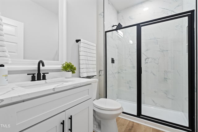 bathroom with a marble finish shower, toilet, and wood finished floors