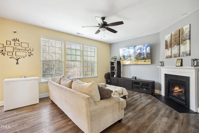 living area featuring visible vents, a ceiling fan, a glass covered fireplace, wood finished floors, and baseboards