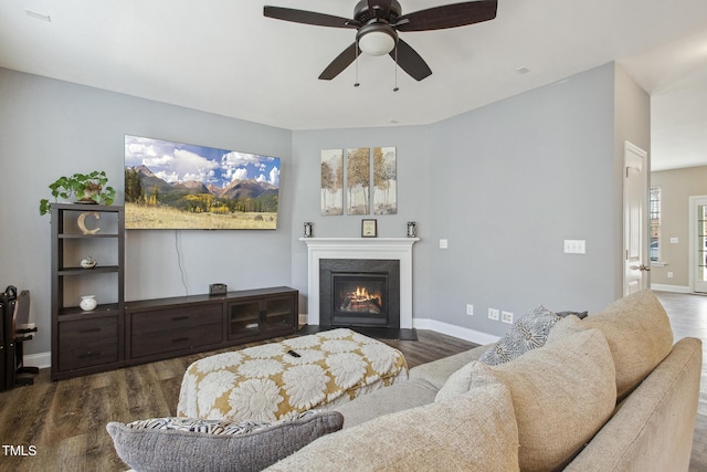 living room featuring a fireplace with flush hearth, wood finished floors, baseboards, and ceiling fan