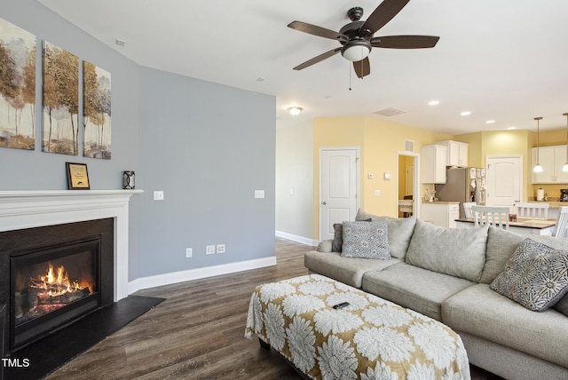 living room featuring dark wood-style floors, baseboards, recessed lighting, ceiling fan, and a glass covered fireplace