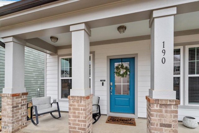 doorway to property featuring a porch and brick siding