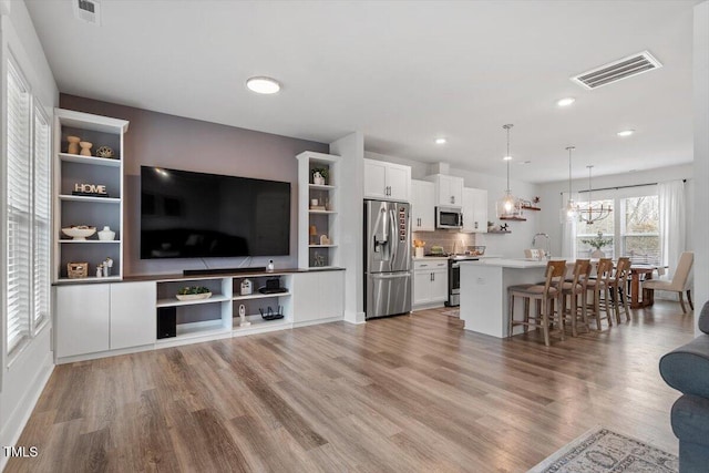 living area featuring recessed lighting, visible vents, an inviting chandelier, and wood finished floors