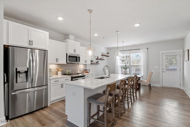 kitchen featuring a center island with sink, decorative backsplash, stainless steel appliances, white cabinetry, and a sink