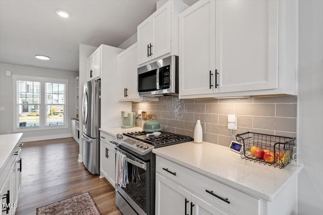 kitchen with light stone counters, backsplash, wood finished floors, white cabinetry, and appliances with stainless steel finishes