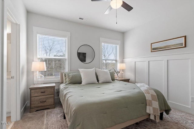 bedroom with visible vents, ceiling fan, carpet, a wainscoted wall, and a decorative wall