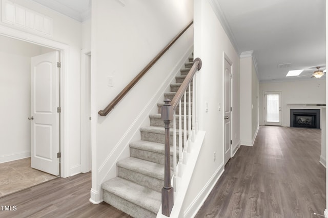 stairs featuring visible vents, wood finished floors, a fireplace, and crown molding