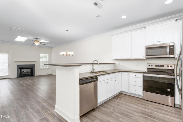 kitchen featuring visible vents, a peninsula, a fireplace, a sink, and stainless steel appliances