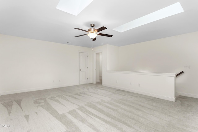 unfurnished room featuring a skylight, light colored carpet, baseboards, and ceiling fan