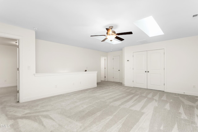 interior space featuring baseboards, light colored carpet, a skylight, and a ceiling fan