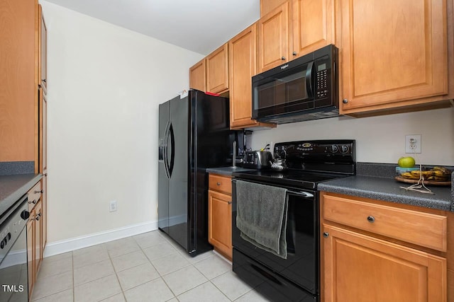 kitchen featuring dark countertops, brown cabinetry, light tile patterned flooring, black appliances, and baseboards