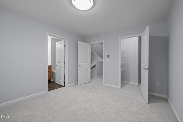 unfurnished bedroom with ensuite bathroom, visible vents, baseboards, a spacious closet, and carpet