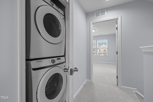 clothes washing area with light carpet, visible vents, stacked washer and clothes dryer, and baseboards