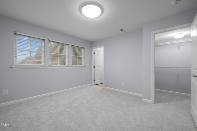 unfurnished bedroom with baseboards, visible vents, a walk in closet, carpet flooring, and a closet