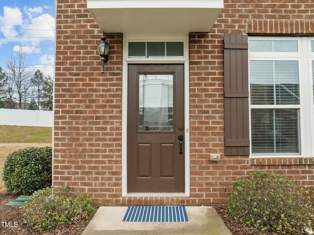 doorway to property featuring brick siding and fence