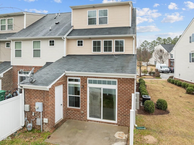 back of house featuring brick siding, fence, roof with shingles, a lawn, and a patio area