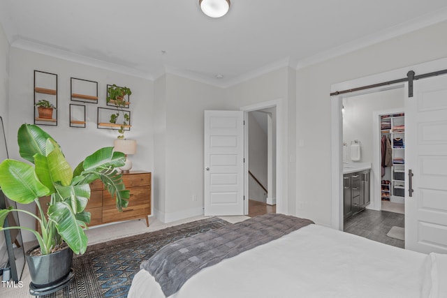 bedroom featuring ornamental molding, wood finished floors, a barn door, baseboards, and a spacious closet