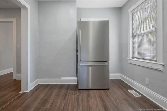 kitchen featuring a textured wall, dark wood-style flooring, visible vents, baseboards, and freestanding refrigerator