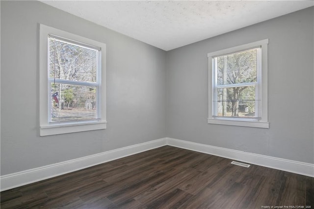 empty room featuring baseboards, dark wood-style flooring, and a wealth of natural light