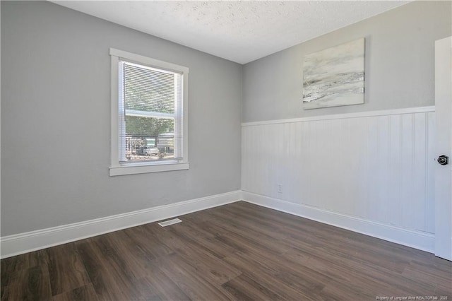 spare room with a wainscoted wall, visible vents, dark wood-type flooring, a textured ceiling, and baseboards