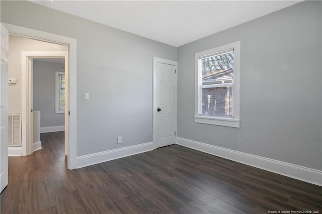 unfurnished bedroom featuring multiple windows, dark wood-style flooring, and baseboards