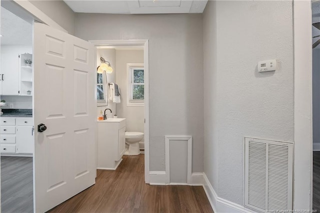 hall with dark wood-type flooring, a sink, visible vents, and baseboards